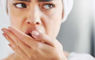 Close-up photo of a concerned person lightly covering their mouth with their hand in a clean, modern bathroom with soft natural light and neutral tones.