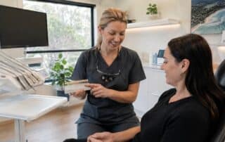 Dentist showing a tooth shade guide to a patient during a professional teeth whitening consultation.